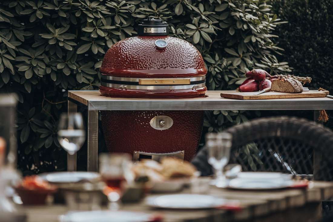 Monolith Kamado Grill Modell .66 auf einer Terrasse, im unscharfen Vordergrund ein reich gedeckter Esstisch